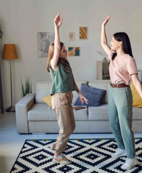 Hilarious mother and teenage daughter dancing in living room while enjoying leisure together